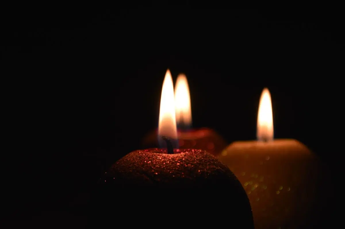 Trois bougies allumées diffusant une lumière chaude sur fond sombre, ambiance élégante et intime