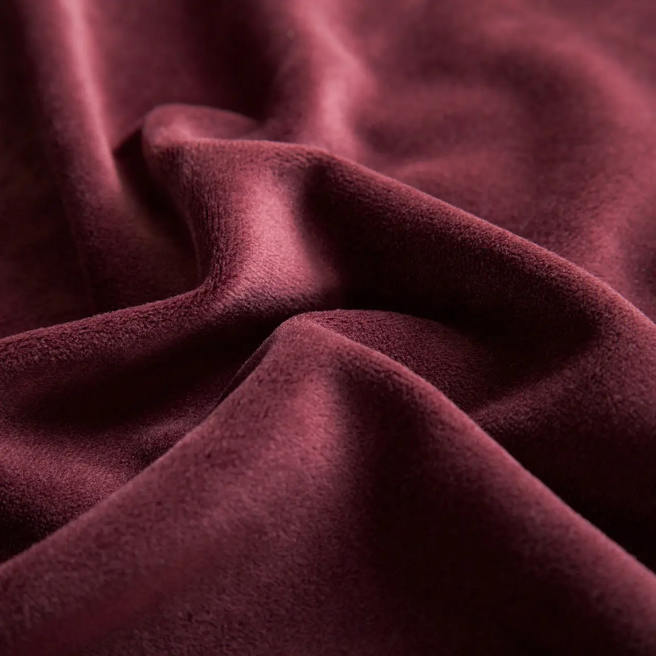 Gros plan sur un tissu de velours bordeaux aux plis doux, ambiance élégante et feutrée